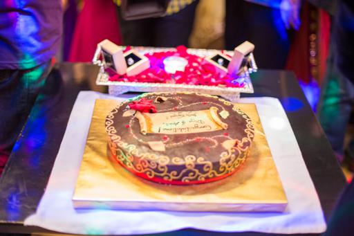 A birthday cake on a table with people surrounding it